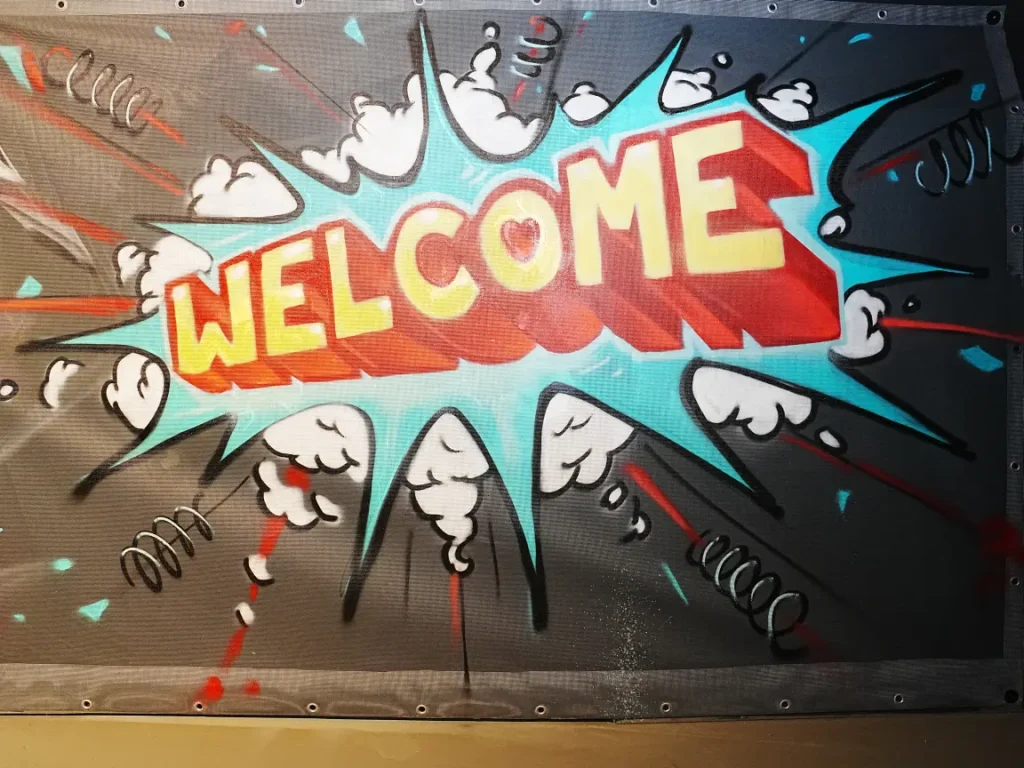 Graffiti-Wand mit großem „Welcome“-Schriftzug in Comic-Stil mit türkisfarbener Sprechblase