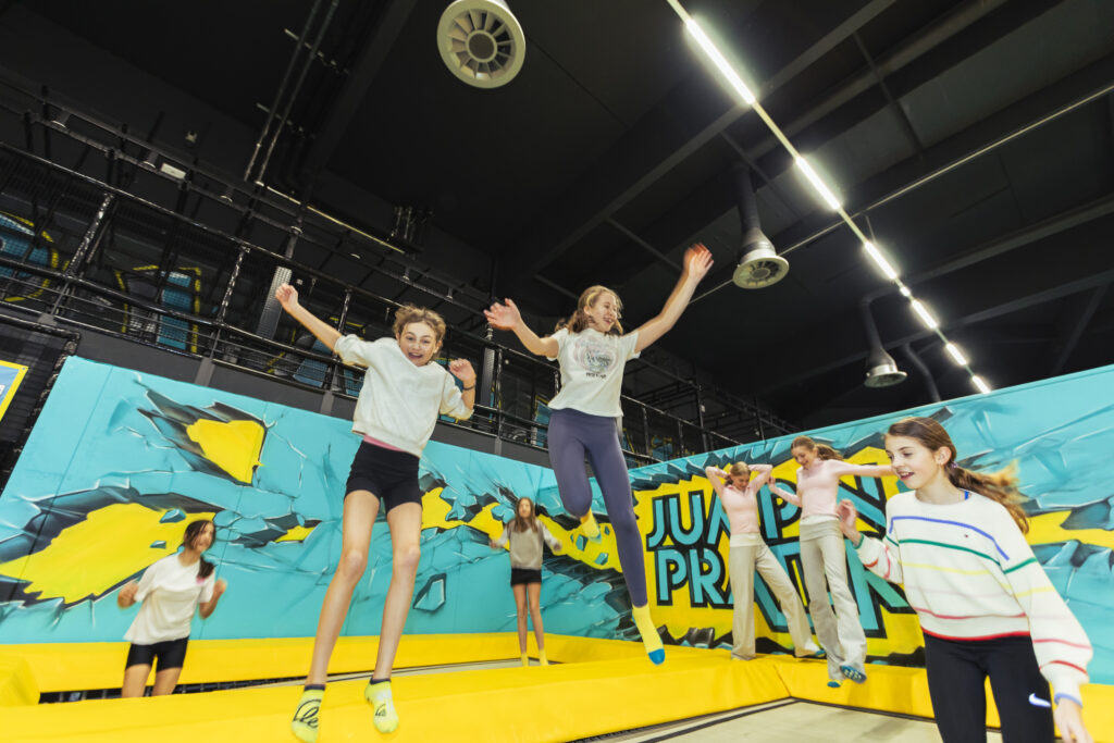 Kinder springen gemeinsam auf Trampolinen in einer Indoor-Trampolinhalle und haben Spaß bei Bewegung und Freizeitaktivitäten.